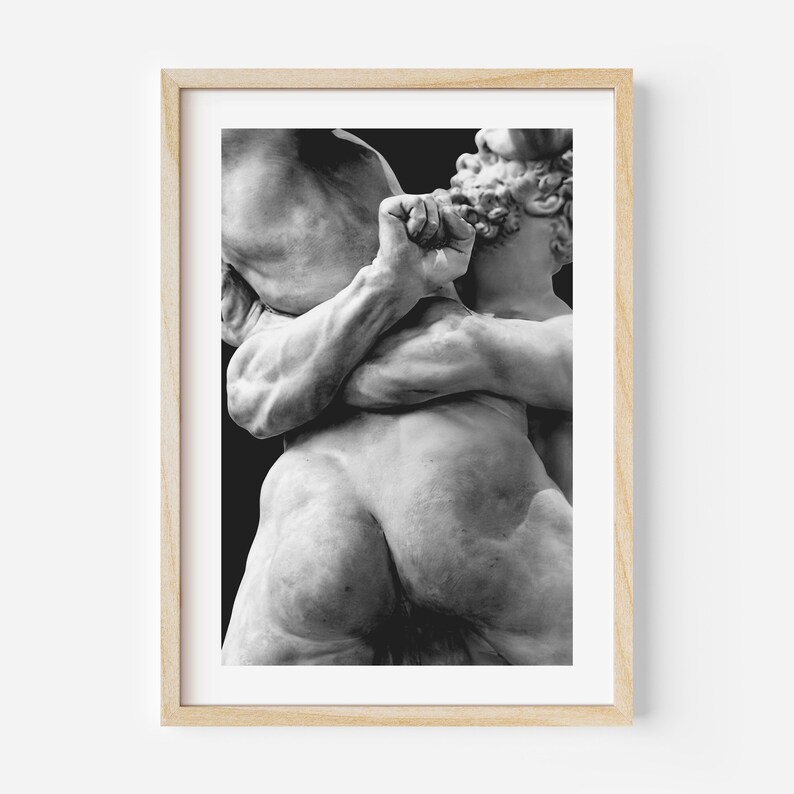 May include: Black and white framed print of a classical sculpture depicting two figures in a dynamic embrace. The sculpture showcases detailed musculature and a dramatic pose, set against a dark background.
