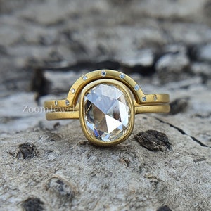 May include: A gold ring featuring a large, oval-shaped diamond set in a bezel setting. The ring is accented with smaller diamonds set in a pave setting around the band. The ring is resting on a piece of wood.