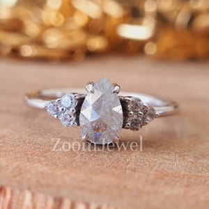 Könnte beinhalten: Ein Verlobungsring mit einem birnenförmigen Diamanten, einem silbernen Band und kleineren Diamanten auf beiden Seiten des Mittelstücks.