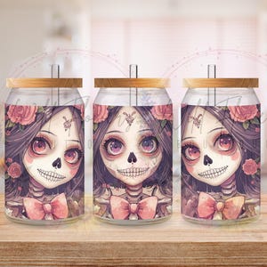 May include: Three glass can-shaped tumblers with bamboo lids. Each features a Day of the Dead-inspired design with a skull face, pink bow, and floral accents. The artwork is in a cartoon style with a soft color palette.