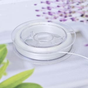 Könnte beinhalten: Eine Spule weißen elastischen Fadens in einem durchsichtigen Plastikbehälter. Der Faden ist um eine zentrale Spule gewickelt.