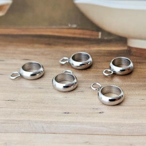 Könnte beinhalten: Fünf silberne Metallringverbinder mit einer Schlaufe an einer Seite. Die Ringe sind glatt und glänzend.