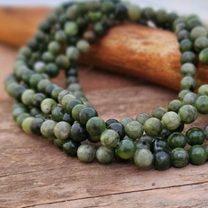 Könnte beinhalten: Nahaufnahme von mehreren Strängen grüner Edelsteinperlen. Die Perlen sind rund und variieren in Grüntönen, von hell bis dunkel. Die Perlen liegen auf einer Holzoberfläche. Die Perlen sind ein Naturstein.