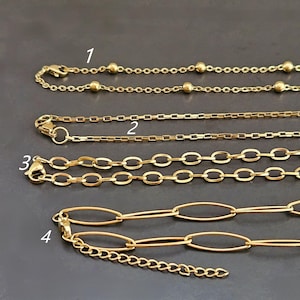 Könnte beinhalten: Vier goldfarbene Halsketten mit unterschiedlichen Gliederstilen. Die Ketten umfassen Kugel-, rechteckige, ovale und länglich-ovale Glieder. Jede Kette hat einen Verschluss. Der Hintergrund ist dunkelgrau.