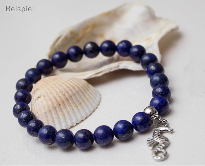 May include: A blue lapis lazuli beaded bracelet with a silver seahorse charm. The bracelet is displayed on a seashell.