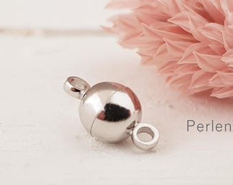 May include: A shiny, silver magnetic clasp with two loops, designed for jewelry making. The clasp is spherical with a visible seam. The background features a soft pink flower and the word "Perlen".