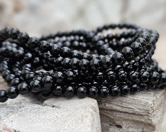 May include: Close-up of several strands of glossy, black beads. The beads are round and uniform in size, reflecting light. The strands are arranged in a layered pattern, creating a sense of depth and texture. The background is a neutral, wooden surface.