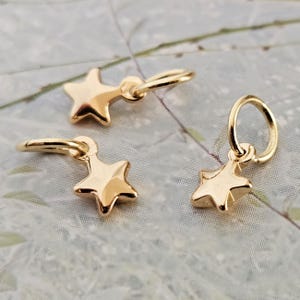 Könnte beinhalten: Drei goldfarbene Stern-Anhänger mit angebrachten Ringen. Die Anhänger sind klein, mit poliertem Finish, und für die Schmuckherstellung oder das Basteln bestimmt. Die Sterne haben ein fünfzackiges Design.