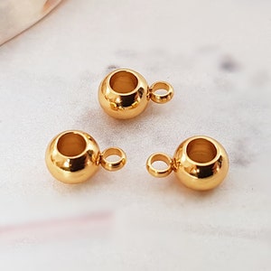 Könnte beinhalten: Drei goldfarbene Metallperlenkappen mit einer kleinen Schlaufe an jeder. Die Perlenkappen sind rund und haben eine hohle Mitte.