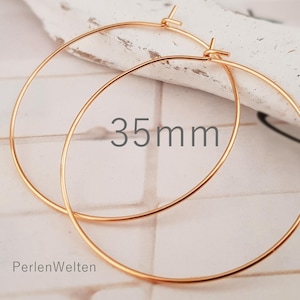 May include: A pair of gold-colored hoop earrings. The earrings are 35mm in diameter. The text "35mm" is displayed on the image. The brand name "PerlenWelten" is also visible.