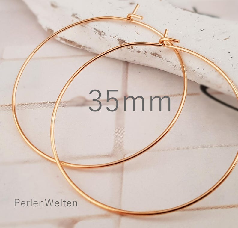 May include: A pair of gold-colored hoop earrings. The earrings are 35mm in diameter. The text "35mm" is displayed on the image. The brand name "PerlenWelten" is also visible.