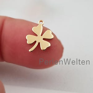 Könnte beinhalten: Goldfarbener Metall-Glücksbringer mit vier Blättern und einer Öse oben zum Anbringen an Schmuck oder Bastelarbeiten.