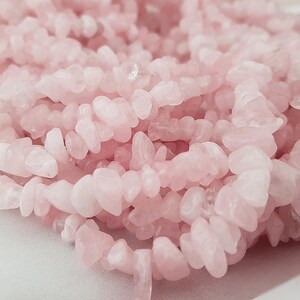 Könnte beinhalten: Eine Schnur rosafarbener Rosenquarz-Chipsteine. Die Steine sind unregelmäßig geformt und haben eine natürliche, getrommelte Oberfläche.
