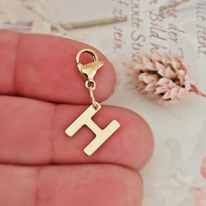 May include: Gold charm with a letter H pendant attached to a lobster clasp.