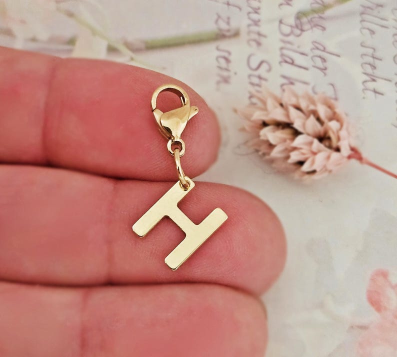May include: Gold charm with a letter H pendant attached to a lobster clasp.