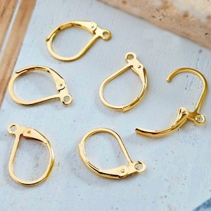 Könnte beinhalten: Nahaufnahme von mehreren goldfarbenen Ohrringverschlüssen mit Bügelverschluss. Die Verschlüsse sind in verschiedenen Positionen zu sehen, was ihr Design und ihre Funktionalität zeigt. Die Ohrringverschlüsse mit Bügelverschluss sind so konzipiert, dass sie Ohrringe sicher befestigen.