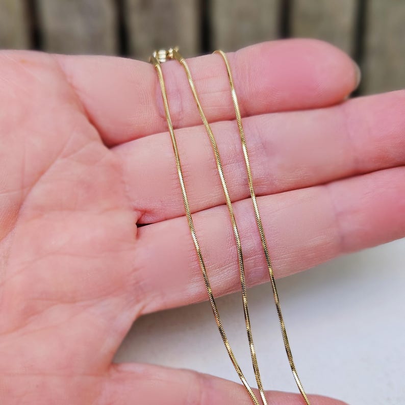 May include: Three gold chains of different lengths, laid out on a hand.