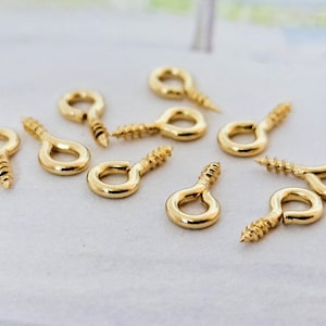 Könnte beinhalten: Nahaufnahme von zehn goldfarbenen Schraubösen. Die Ösen sind klein und haben ein schlichtes Design.