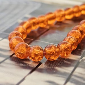 Könnte beinhalten: Eine Kette aus bernsteinfarbenen, runden Perlen. Die Perlen sind durchscheinend mit sichtbaren inneren Strukturen. Die Perlen sind aufgereiht und bilden eine gebogene Linie vor einem verschwommenen Hintergrund.