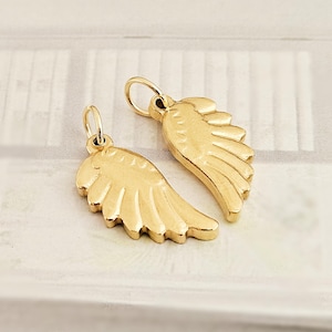 May include: Two gold-colored wing charms with a loop at the top for hanging. The charms are detailed with feather-like lines and have a polished finish. The wings are a symbol of freedom and protection.