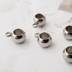 May include: Five silver metal bead caps with a small loop on top. The bead caps are round and have a smooth, shiny finish.