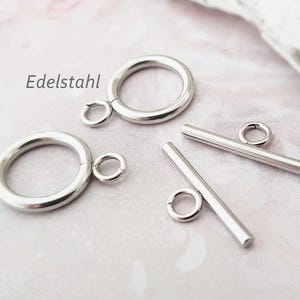 Könnte beinhalten: Ein Satz silberfarbener Metallschließen für Schmuck, darunter zwei runde Ringe mit jeweils einem kleineren Ring und zwei Toggle-Verschlüsse mit einer Stange und einem Ring.