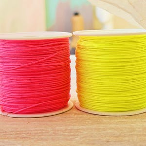 Könnte beinhalten: Zwei Spulen mit leuchtend farbigem Kordel. Eine Spule ist ein leuchtendes Pink, die andere ein leuchtendes Gelb. Die Kordel ist eng auf weißen Spulen aufgewickelt. Das Bild ist eine Nahaufnahme, die die Textur und Farbe der Kordel zeigt.