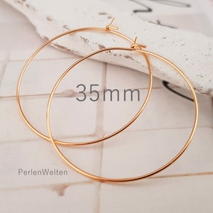 May include: A pair of gold-colored hoop earrings. The earrings are 35mm in diameter. The text "35mm" is visible on the image. The brand name "PerlenWelten" is also visible.