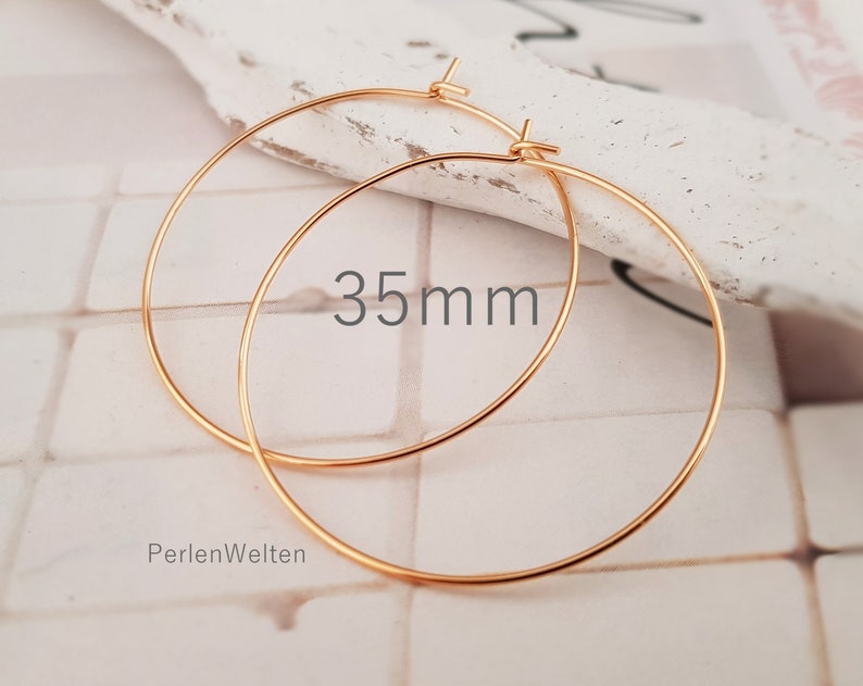May include: A pair of gold-colored hoop earrings. The earrings are 35mm in diameter. The text "35mm" is visible on the image. The brand name "PerlenWelten" is also visible.