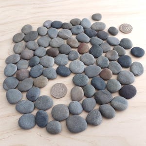 May include: A white ceramic mug with a black handle and the text "But First, Coffee" in a bold, black font. The mug is set against a blurred background, suggesting a cosy setting.