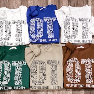 May include: Five different colored sweatshirts with the letters "OT" made up of small occupational therapy symbols. The text "Occupational Therapy" is printed below the letters.