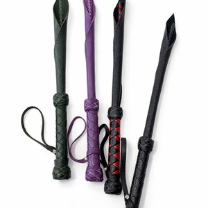Puede incluir: Cuatro l&aacute;tigos de cuero en tonos verde, morado, negro y rojo. Cada l&aacute;tigo presenta un mango trenzado y un lazo para la mu&ntilde;eca. Las puntas est&aacute;n dobladas y cosidas, creando un dise&ntilde;o &uacute;nico. Los l&aacute;tigos se muestran sobre un fondo blanco.