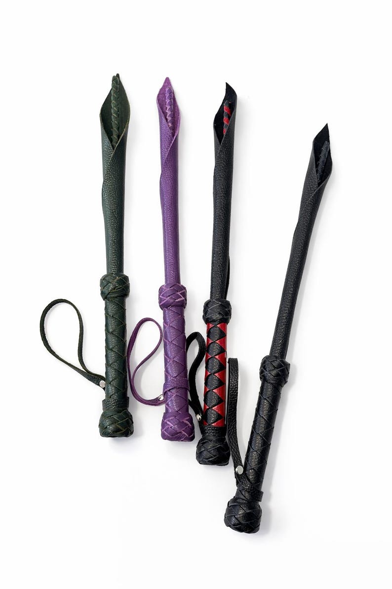 Puede incluir: Cuatro l&aacute;tigos de cuero en tonos verde, morado, negro y rojo. Cada l&aacute;tigo presenta un mango trenzado y un lazo para la mu&ntilde;eca. Las puntas est&aacute;n dobladas y cosidas, creando un dise&ntilde;o &uacute;nico. Los l&aacute;tigos se muestran sobre un fondo blanco.