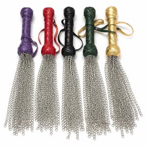 May include: Five colorful whips with chain tassels. The handles are in purple, red, black, green, and gold. Each handle has a braided design and a wrist strap. The chain tassels are made of silver-colored metal.