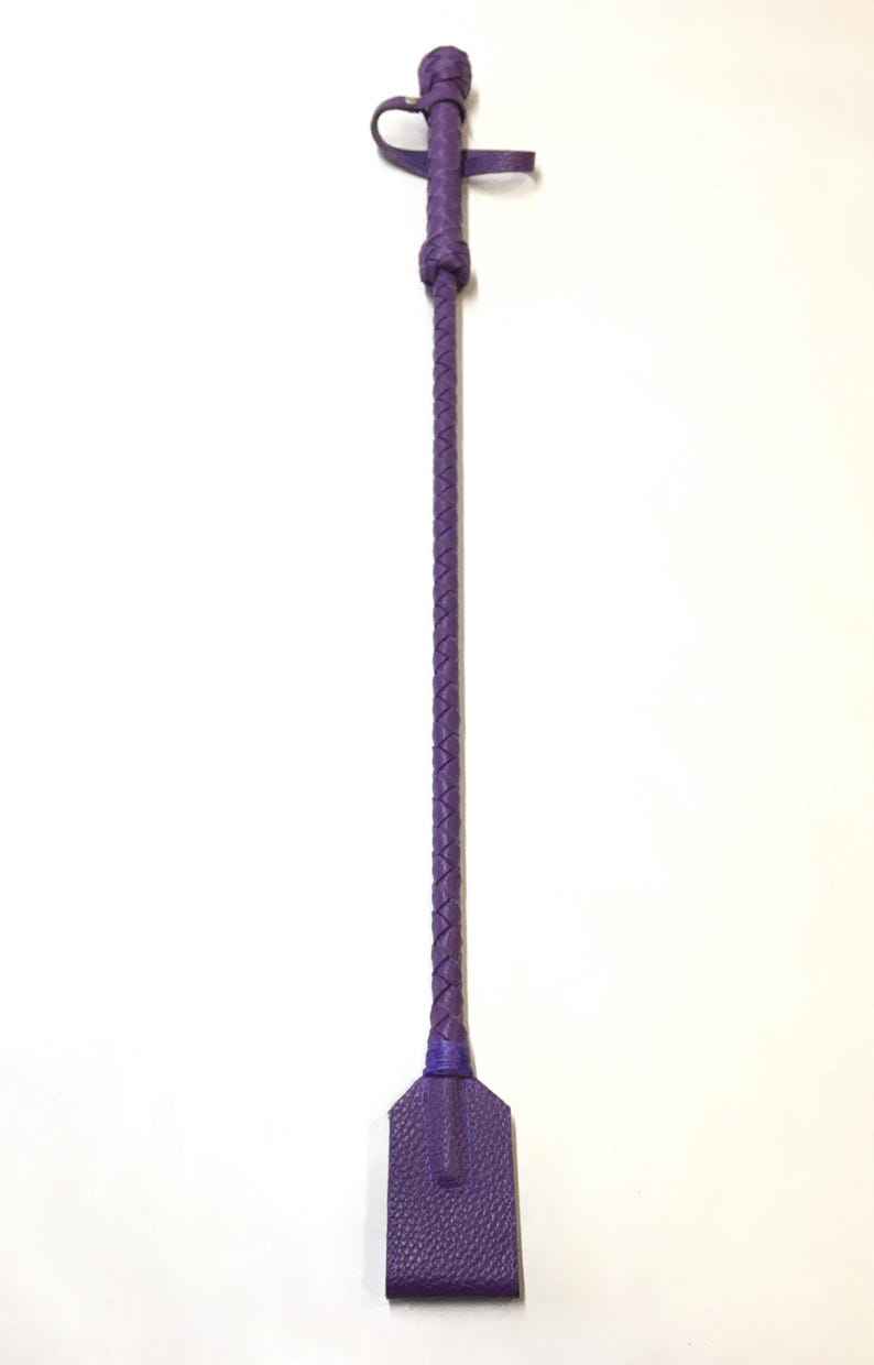 May include: A purple leather riding crop with a braided handle and a flat, rectangular paddle.