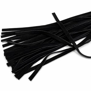 May include: A close-up shot of a collection of black suede leather strips. The strips are thin and rectangular, with a soft, matte texture. The leather is a deep, solid black colour, and the strips are arranged in a slightly overlapping pattern.