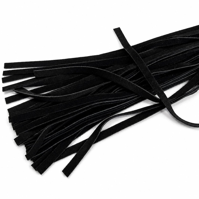May include: A close-up shot of a collection of black suede leather strips. The strips are thin and rectangular, with a soft, matte texture. The leather is a deep, solid black colour, and the strips are arranged in a slightly overlapping pattern.