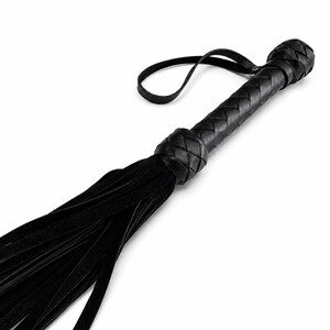 May include: A black leather whip featuring a braided handle and a loop. The whip's body is composed of numerous long, thin leather strips.