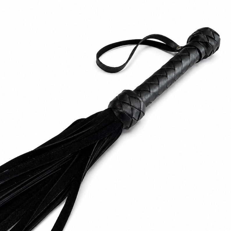 May include: A black leather whip featuring a braided handle and a loop. The whip's body is composed of numerous long, thin leather strips.