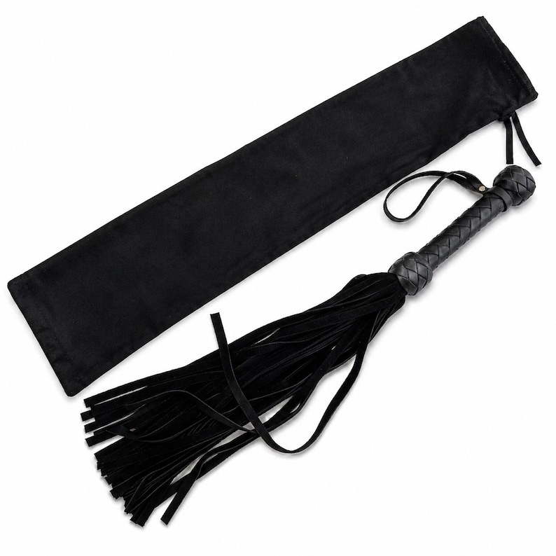 May include: Black leather flogger with a braided handle and long, flowing fringe. It includes a matching black storage bag. The handle has a loop for hanging. The design is simple and elegant.