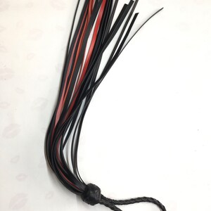 May include: A black and red leather flogger with a braided handle and a knotted base. The flogger features multiple leather falls in black and red, and is designed for impact play.