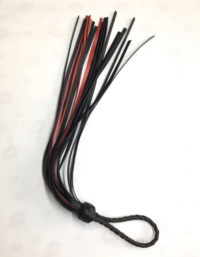 May include: A black and red leather flogger with a braided handle and a knotted base. The flogger features multiple leather falls in black and red, and is designed for impact play.