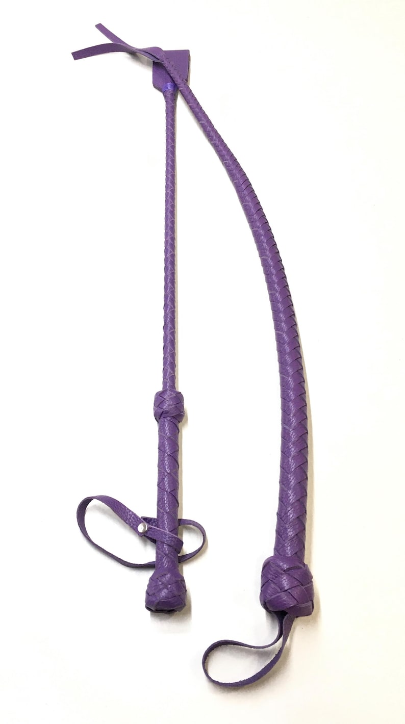May include: Two purple leather whips with braided handles and straps. The whips are made of a soft, supple leather and have a classic design.