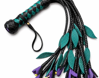 May include: A braided leather flogger featuring a handle with a black and teal crisscross pattern and a wrist strap. The tails consist of multiple black braided strands adorned with teal leather leaves and purple flower blossoms with yellow centers.
