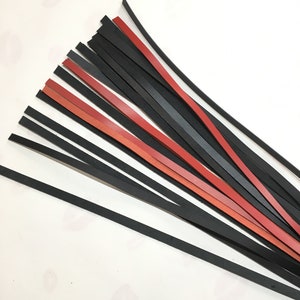 May include: A bundle of leather strips in black, red, and gray. The strips are thin and appear to be cut from a larger piece of leather. The strips are arranged in a fan-like pattern, with some overlapping others.