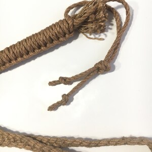 May include: A brown jute rope whip with a braided handle and a knotted end. The rope is thick and has a rough texture.