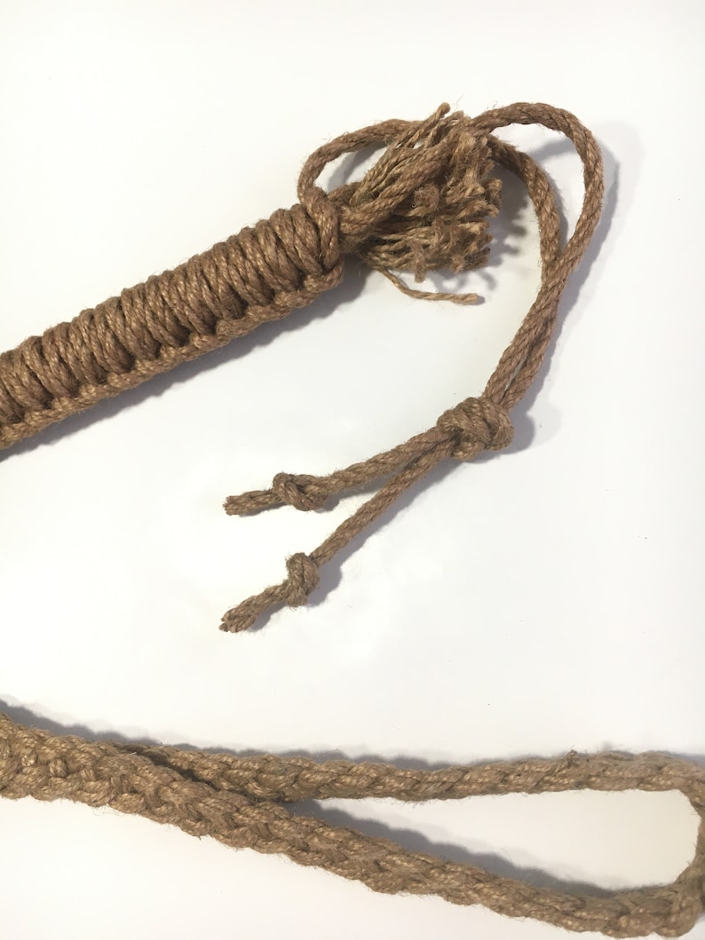 May include: A brown jute rope whip with a braided handle and a knotted end. The rope is thick and has a rough texture.