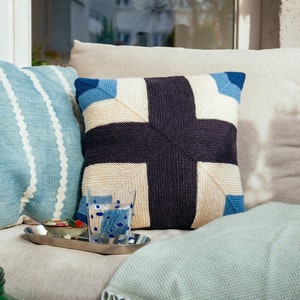 May include: A light blue and white striped cushion, a cream and blue patterned cushion, and a light blue throw blanket on a light beige sofa.