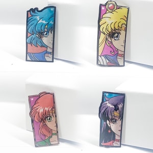 Op de afbeelding: Vier kleurrijke anime-personage stickers met Sailor Moon-personages. Elke sticker is rechthoekig en heeft een ander personage met een roze, blauwe, gele of paarse achtergrond.