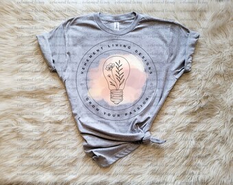 May include: A heather gray t-shirt featuring a circular design with the text "VEHEMENT LIVING DESIGNS" and "GROW YOUR PASSION". The design includes a lightbulb with flowers inside, set against a pink and peach background.